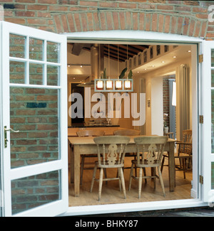 View through open French windows of dining room extension with pine chairs and table Stock Photo
