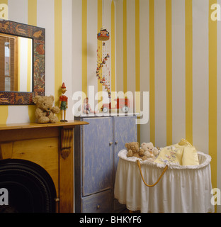 Wide-striped yellow wallpaper and blue cupboard in nursery bedroom with baby's cot with white muslin trim Stock Photo