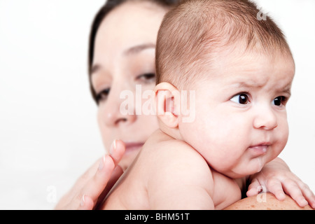 Beautiful Caucasian Hispanic Latina mother holding drooling baby over shoulder and tapping on back so infant can burp, isolated. Stock Photo
