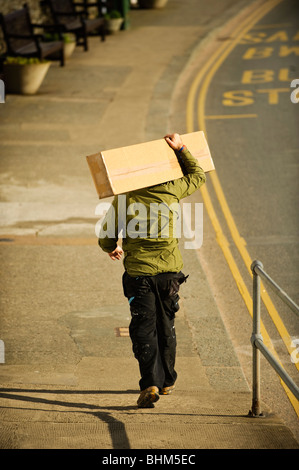 A man carrying a large package on his shoulders, back walking down the street, UK Stock Photo