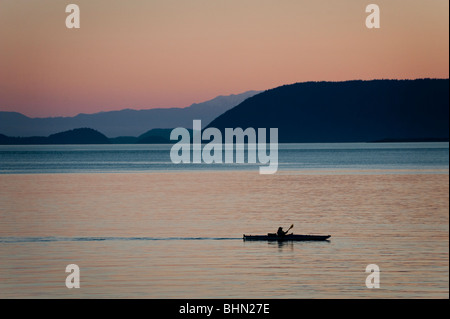 A kayaker, at sunset, paddles between Lummi Island and Orcas Island in the San Juan Islands of Washington State. Stock Photo