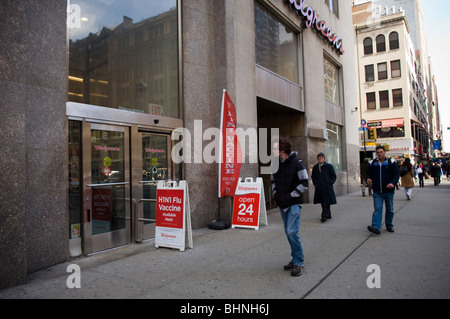 Pedestrians pass a sign saying H1N1 flu shots available outside a Walgreen 's pharmacy in the Murray Hill neighborhood of NY Stock Photo