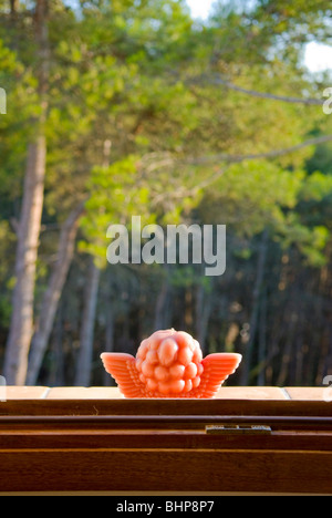 a close up of rear of red cupid candle on a window sill glowing in the sun with forest in the background Stock Photo