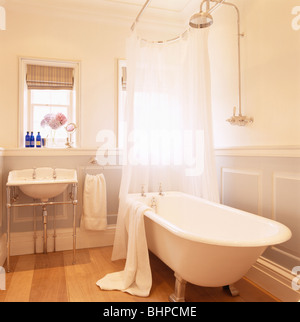 Chrome shower on wall above roll-top bath with white shower curtains in modern white townhouse bathroom Stock Photo