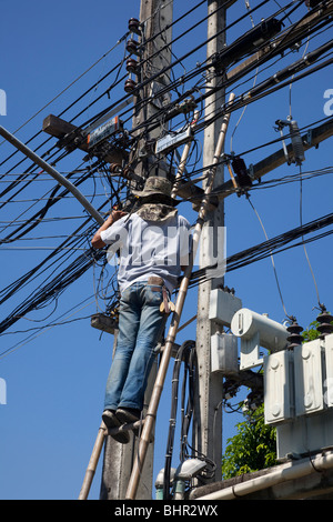 Electrician repairing electricity supply on overhead cabling; domestic wiring in Chiang Mai Thailand, without protective gear or equipment. Stock Photo