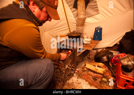 A MAN LIGHTS A FIRE INSIDE A HEATED WINTER CAMPING TENT STOVE Stock Photo