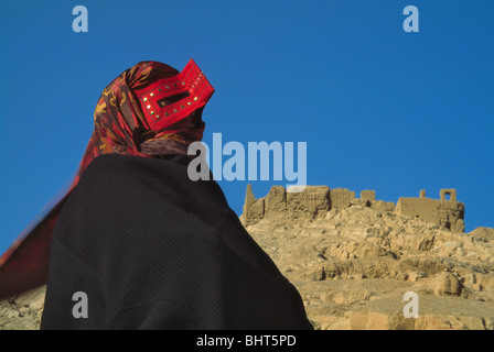 Bandari woman wearing a burqa and red mask with ruins of the Fire Temple, Esfahan, Iran Stock Photo