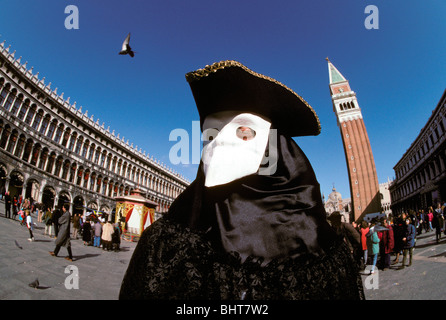 Man in black carnival costume & hat & white mask in San Marco Square, showing San Marco Campanile in background Stock Photo