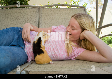 Portrait 10-11 year old girl relaxes relaxing playing with her Guinea pig on outside swing. United States  MR  © Myrleen Pearson Stock Photo