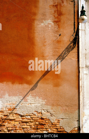 Shadow of street lamp on faded pastel red ochre coloured wall in Venice street, late afternoon Stock Photo