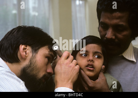 A young national Health general practitioner doctor (GP) uses an otoscope to inspect a young little girl Stock Photo