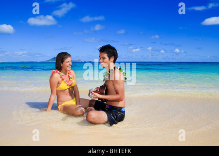 pacific island man plays his ukulele for a young woman on a hawaii beach Stock Photo