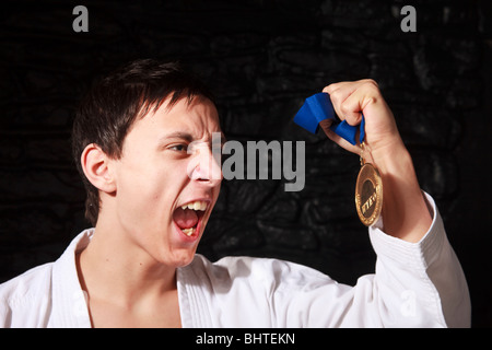 male Karate champion showing off gold medal won in competition with victorious look on face Stock Photo