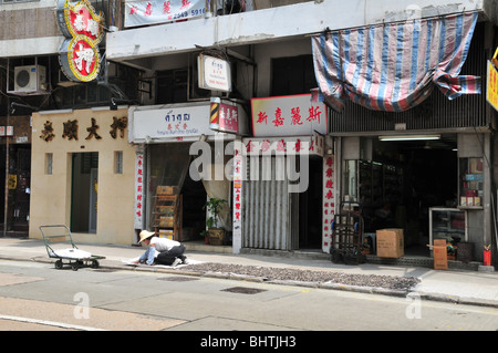 Woman in a bamboo hat spreading seafood to dry in the sun on a pavement outside shops, Queen's Road West, Hong Kong, China Stock Photo