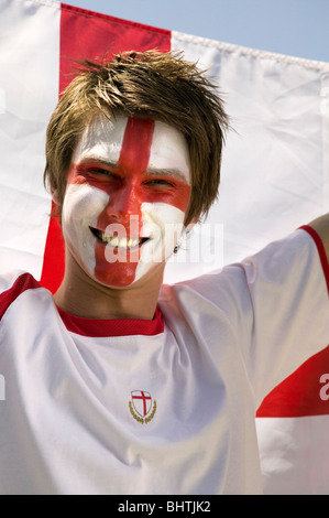 a cheering England football supporter with the St. George's flag painted on his face holding up the England flag Stock Photo