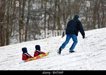 Father Pulling Two Young Children Up Hill on Sled in Cherokee Park in Louisville Stock Photo