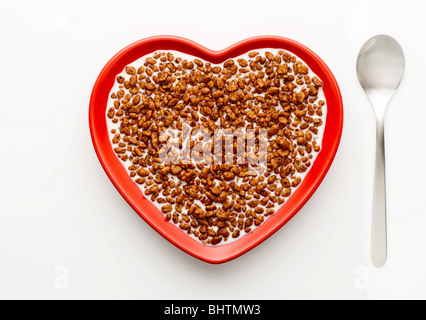 Studio shot of red heart shaped bowl of coco pops and milk with a spoon,on a white background, shot from above. Stock Photo