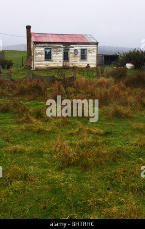 A rundown cottage in isolated countryside with an out of place television satellite dish mounted on wall. Stock Photo
