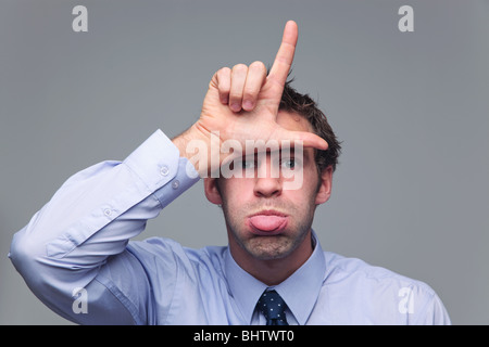 Man in shirt and tie sticking his tongue out and making the letter L with his hand known as the hand gesture for loser Stock Photo