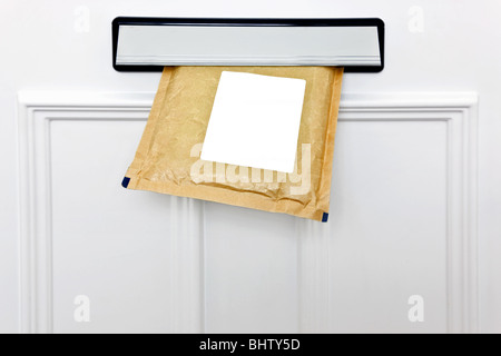 A padded envelope in the letterbox of a white front door, blank label for you to add your own name and address. Stock Photo