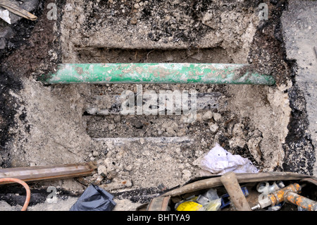 Old metal gas pipe visible below the green fiber optic pipe. Stock Photo