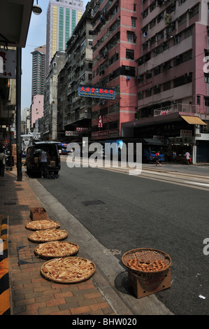 Shops, delivery lorries and bamboo trays of seafood drying in the sun on the pavement edge of Des Voeux Road West, Hong Kong, Stock Photo