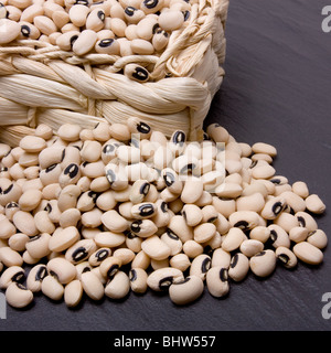 Black eyed peas overflowing from wicker basket against dark slate. Stock Photo
