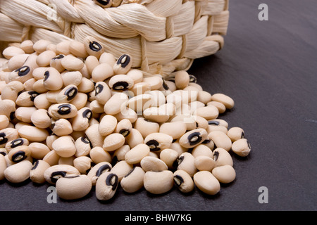 Black eyed peas overflowing from wicker basket against dark slate. Stock Photo