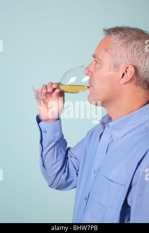 Man in a blue shirt drinking a glass of white wine Stock Photo