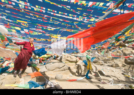 A Buddhist monk standing next to prayer flags in Tibet Stock Photo