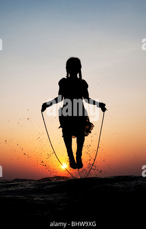 Silhouette of a young Indian girl skipping in water at sunset. India Stock Photo