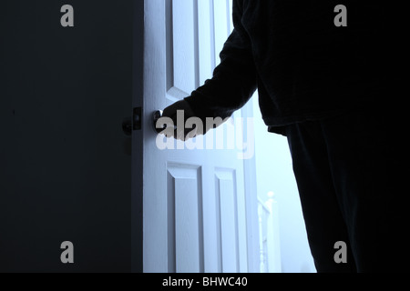 Man's hand turning the door handle, as he enters a dark room Stock Photo