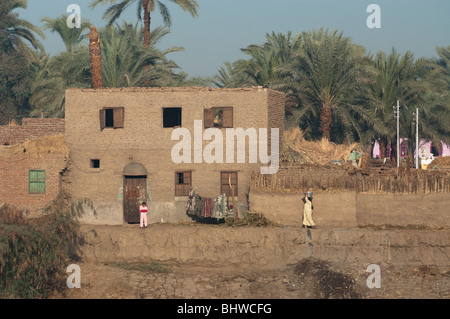 View of houses on bank of the river Nile, near Luxor, Egypt with local people in colourful clothes and a woman carrying water Stock Photo