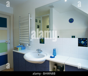 Radiator on wall beside mirror above basin set into blue vanity unit with white worktop in modern white bathroom Stock Photo