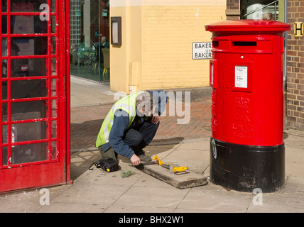 An electrical engineer repairing wiring probably telephone wire beneath a pavement  in Uxbridge West London UK Stock Photo