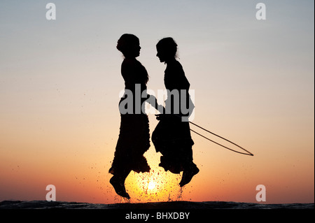 Silhouette of young Indian girls skipping in water at sunset. India Stock Photo