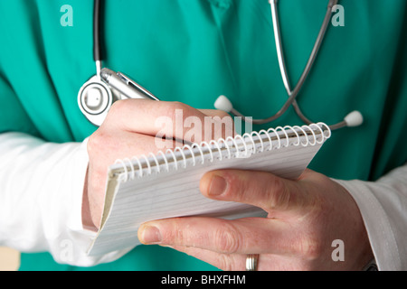 man wearing medical scrubs and stethoscope writing notes in a notebook Stock Photo