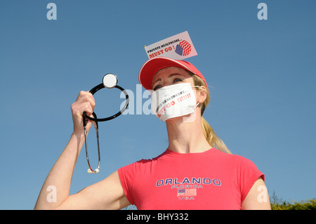 Private healthcare in the USA must go female protester wearing a medical face mask and holding a stethoscope Stock Photo