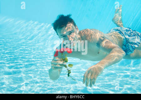 Man swimming with open eyes underwater in pool holding flower Stock Photo