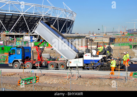 Close up of tipper lorry truck tipping tarmac into road laying machine new road at 2012 Olympic Stadium building construction site Stratford London UK Stock Photo