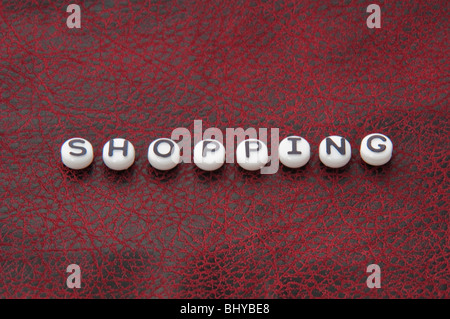The word shopping is part of this series on black and white round lettering beads on a black and red leather textured surface. Stock Photo