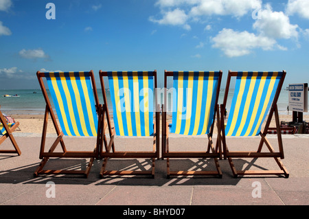 Row of blue and yellow striped deck chairs on the promenade next to Weymouth beach in Dorset Stock Photo