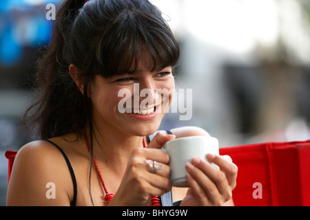 mid twenties hispanic woman smiling over a cup of coffee at an outdoor street cafe Stock Photo