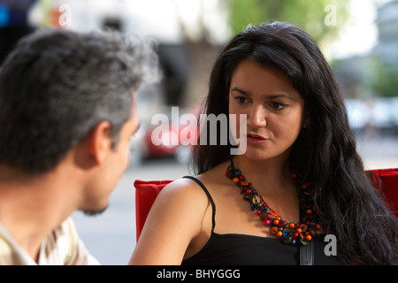 mid twenties hispanic woman in conversation with her male partner at an outdoor cafe table Stock Photo
