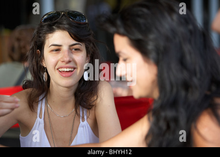 mid twenties hispanic woman talking to her friend at outdoor street cafe table Stock Photo