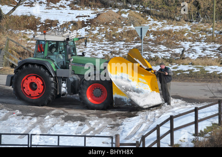 A man shovels off frozen snow from a tractor snow plow / plough. Stock Photo