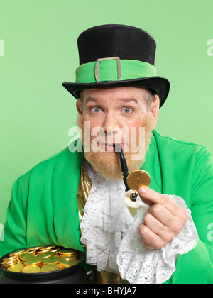 Leprechaun in bright green clothes holding a golden coin in his hand Stock Photo