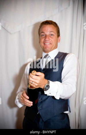 Groom popping cork on champagne bottle Stock Photo