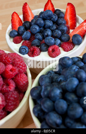 A bowl of healthy breakfast strawberries, raspberries and blueberries in plain yogurt with bowls of raspberries and blueberries Stock Photo