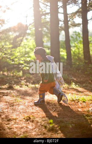 Young boy carrying a blanket in the woods. Stock Photo